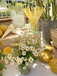 flowers and lemons sit on a table with paper straws in vases next to them