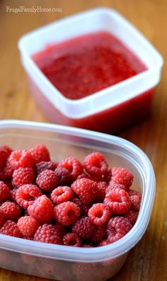 raspberries in a plastic container next to a bowl of red sauce on a wooden table