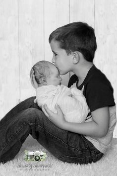 a black and white photo of a young boy kissing a baby