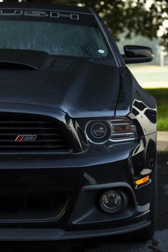 the front end of a black car parked in a parking lot next to a tree