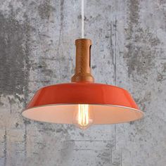 an orange pendant light hanging from a ceiling fixture in a room with concrete walls and cement flooring