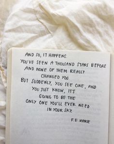 an open book sitting on top of a bed covered in white sheets with writing underneath it