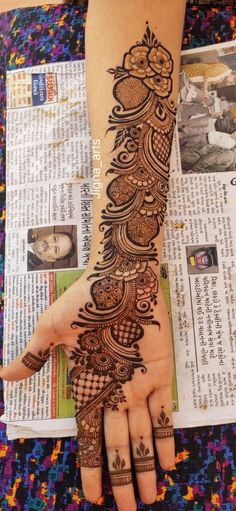 a woman's hand with henna tattoos on it and newspaper pages in the background