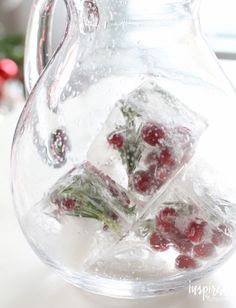 a pitcher filled with ice and cranberries on top of a white table next to a christmas tree