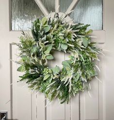 a wreath is hanging on the front door with greenery and white flowers in it