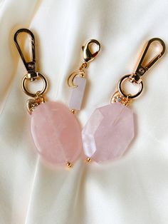 two key chains with pink stones hanging from them on a white fabric background, one is gold and the other is silver