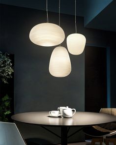 three lights hanging over a table with two cups on it and one light above the table