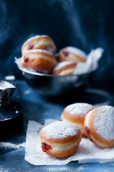 powdered sugar covered donuts sitting on top of wax paper next to other pastries