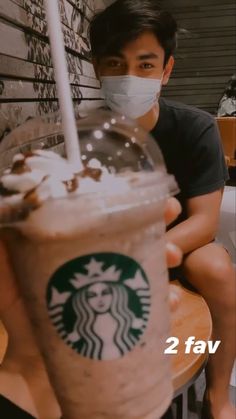 a man wearing a face mask sitting in front of a starbucks drink with the words 2 fav on it