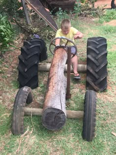 a young boy sitting on top of a wooden log next to large tires and chains