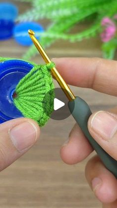 a person holding a crochet hook with yarn on it and another needle in the background