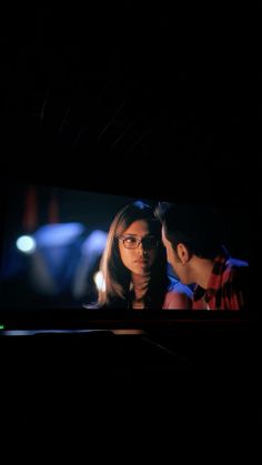 a man standing next to a woman in front of a large screen tv at night