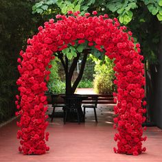 a red archway with flowers on it in the middle of a patio area next to a picnic table