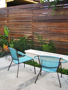 two blue chairs sitting next to each other near a table and bench in front of a wooden fence