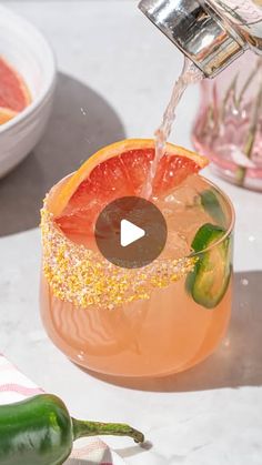 an orange drink being poured into a glass with a slice of grapefruit on the rim