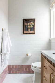 a white toilet sitting next to a sink in a bathroom under a painting on the wall