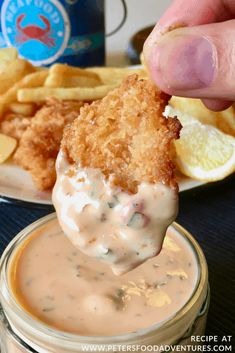 a person dipping some food into a small bowl with fries and dip sauce on the side