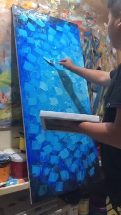 a young boy is painting on an easel with blue paint and glass shards in the background