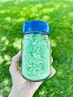 a hand holding a jar filled with green slim ring filaments in the grass