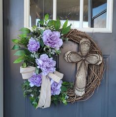 a wreath with purple flowers and a cross hanging on the front door to a house