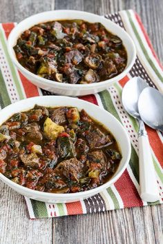 two bowls filled with stew on top of a red and green table cloth next to spoons