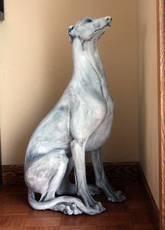 a statue of a dog sitting on top of a wooden floor next to a wall