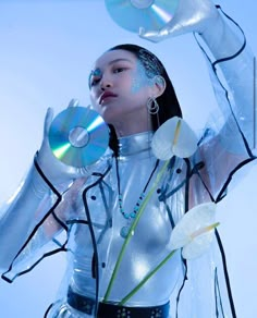 a woman in silver is holding two cd's up to her face with both hands