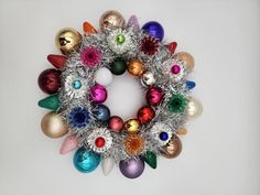 a wreath made up of christmas balls and tinsels on a white table top