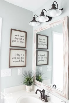 a bathroom sink sitting under a mirror next to two framed pictures and a potted plant