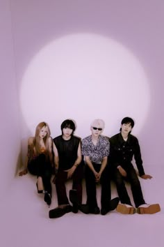 four people sitting on the floor in front of a white wall with a light shining through them