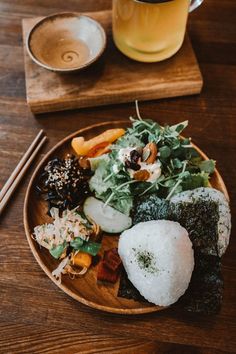 a wooden plate topped with lots of food next to chopsticks and a drink