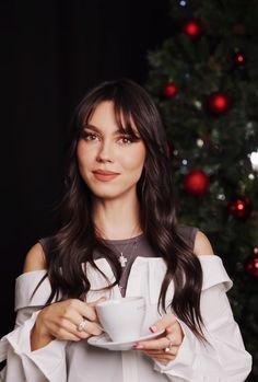 a woman holding a cup in front of a christmas tree