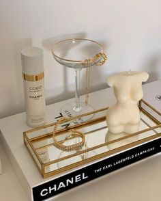 a white table topped with a glass tray filled with perfume bottles and bracelets next to a bottle of chanel