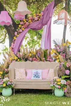 a couch sitting in the middle of a lush green field next to flowers and umbrellas