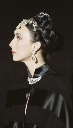 a woman in a black dress and earrings looking off into the distance with her hand on her hip