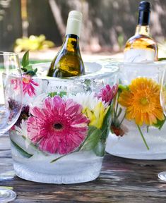 three wine glasses with flowers in them sitting on a table next to two bottles of wine