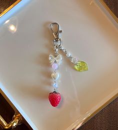 a white tray with a strawberry charm on it and a green heart hanging from the side