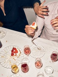 two people sitting at a table with wine glasses and desserts on the table in front of them