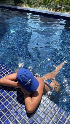 a woman laying on the side of a swimming pool next to a blue tiled wall