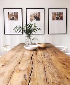 a wooden table topped with two white bowls filled with flowers next to pictures on the wall