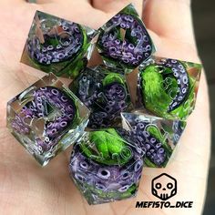 a hand holding some purple and green dices in it's left hand with an octopus on them