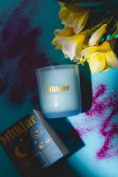 a blue vase with yellow flowers next to it and a tin of lipstick on the table