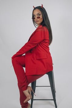 a woman sitting on top of a stool wearing a red suit and devil horns in front of her face