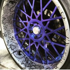 a purple wheel on a white car with graffiti all over the tires and rims