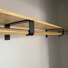 two wooden shelves with black metal brackets on the top and bottom, against a white wall