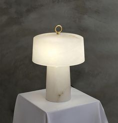 a white table lamp sitting on top of a white cloth covered table next to a gray wall