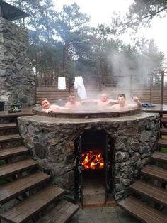 three people in a stone hot tub with wood steps leading up to the fire place