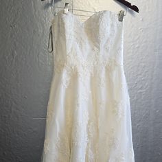 a white dress hanging on a hanger in front of a gray wall with clothes pins attached to it