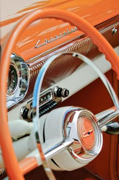 the steering wheel and dashboard of an orange classic car with chrome spokes on it