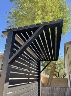 a wooden structure in the middle of a yard next to a tree and fence with a blue sky behind it